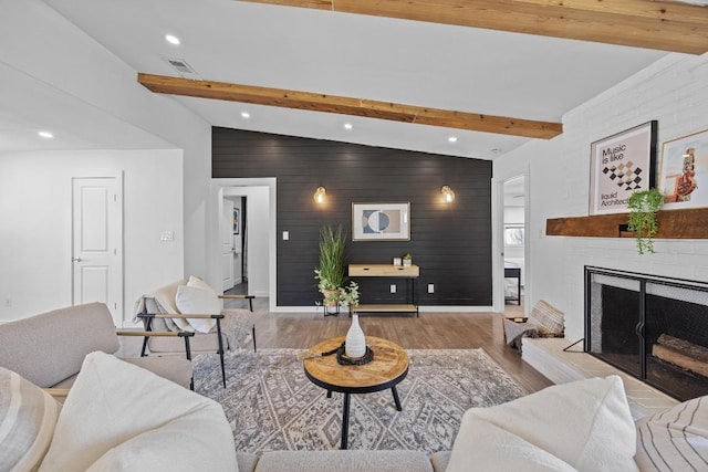 living room featuring lofted ceiling with beams, a large fireplace, an accent wall, wood finished floors, and visible vents