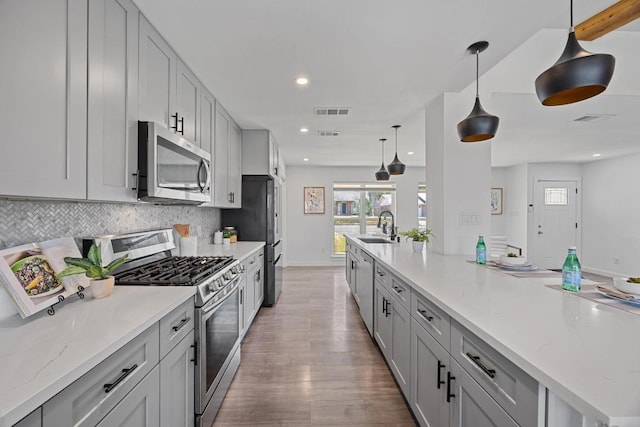 kitchen featuring visible vents, backsplash, appliances with stainless steel finishes, a sink, and wood finished floors