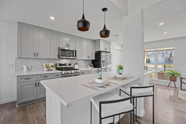 kitchen with appliances with stainless steel finishes, dark wood-type flooring, decorative backsplash, and gray cabinetry