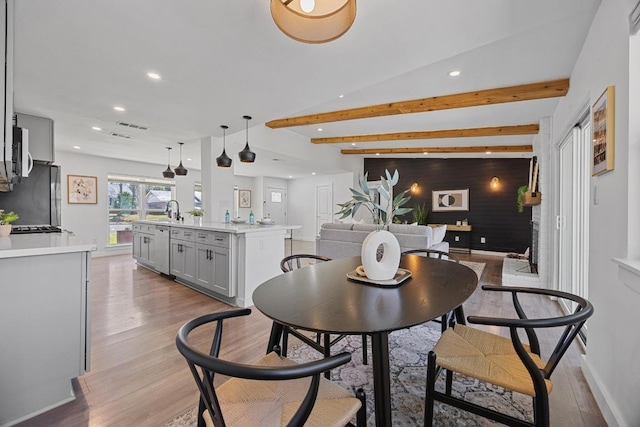 dining space with light wood-type flooring, an accent wall, beamed ceiling, and recessed lighting