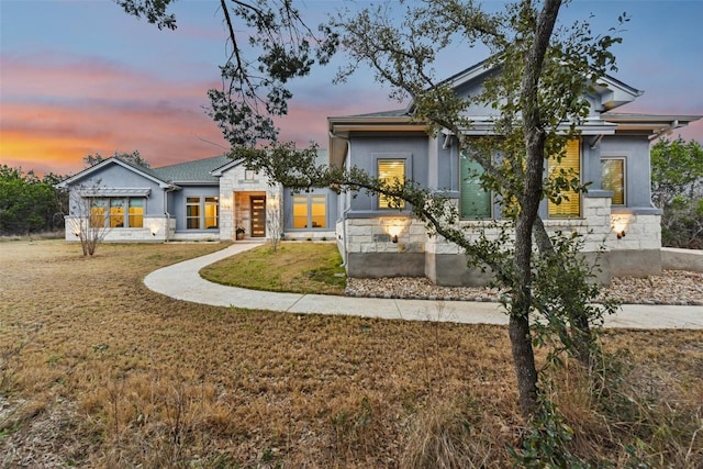 view of front facade featuring a front yard, stone siding, and stucco siding