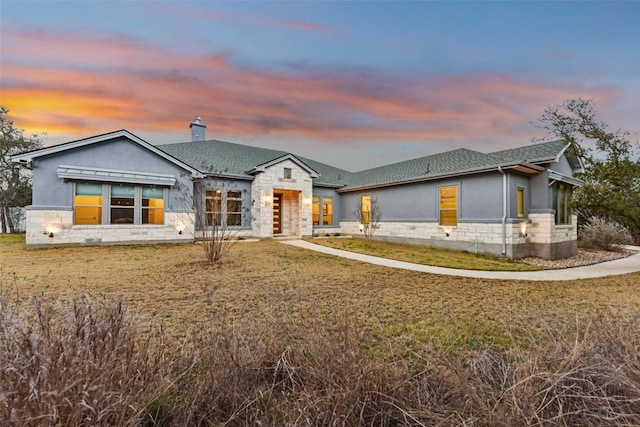 view of front of house featuring a front yard, stone siding, a chimney, and stucco siding