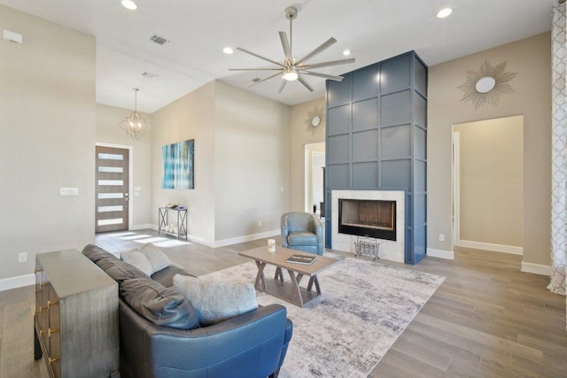 living room featuring baseboards, light wood-type flooring, a tiled fireplace, and recessed lighting