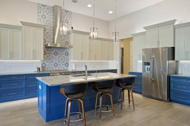 kitchen with light wood-style flooring, appliances with stainless steel finishes, a sink, blue cabinets, and wall chimney exhaust hood