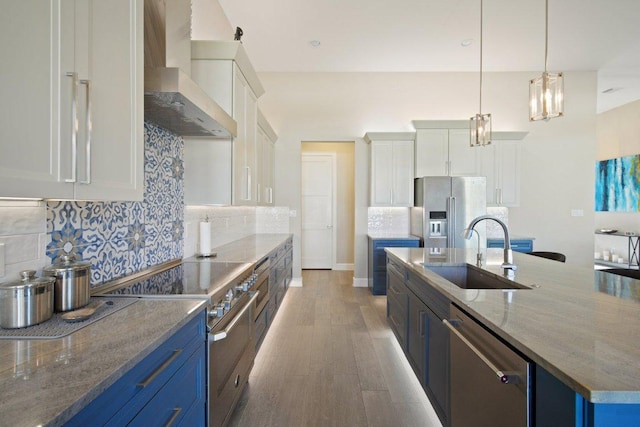 kitchen featuring wall chimney exhaust hood, blue cabinets, a sink, and stainless steel appliances