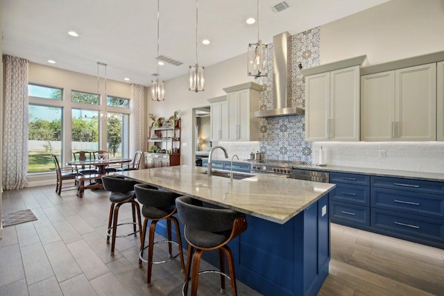 kitchen with blue cabinets, a sink, visible vents, wall chimney range hood, and backsplash