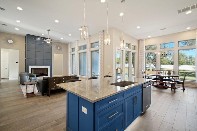 kitchen with blue cabinetry, visible vents, a large fireplace, open floor plan, and a sink