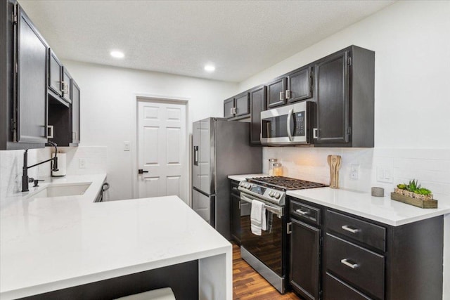 kitchen with dark wood-style flooring, a sink, light countertops, appliances with stainless steel finishes, and tasteful backsplash