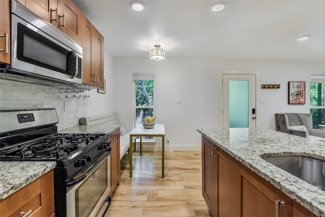 kitchen featuring brown cabinetry, decorative backsplash, light wood-style flooring, light stone counters, and stainless steel appliances