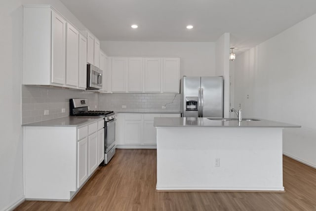 kitchen with stainless steel appliances, tasteful backsplash, white cabinets, a sink, and light wood-type flooring