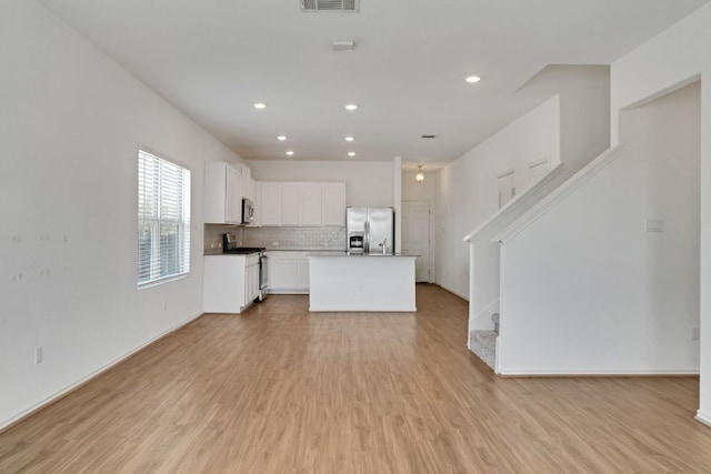 kitchen with tasteful backsplash, visible vents, white cabinets, light wood-style flooring, and stainless steel appliances