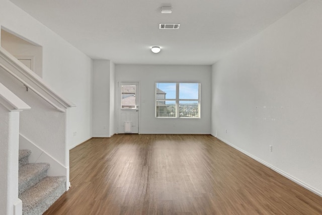 unfurnished living room with stairs, wood finished floors, visible vents, and baseboards