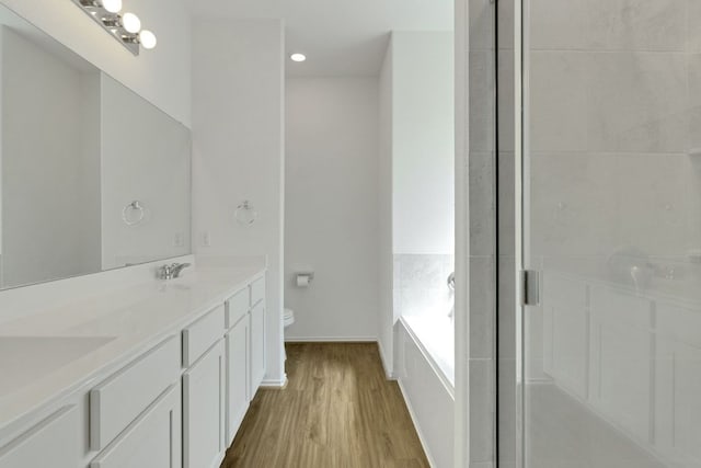 bathroom with double vanity, toilet, a stall shower, wood finished floors, and a bath