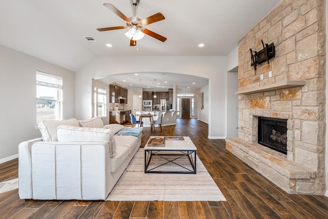 living area with arched walkways, visible vents, dark wood-type flooring, a ceiling fan, and vaulted ceiling