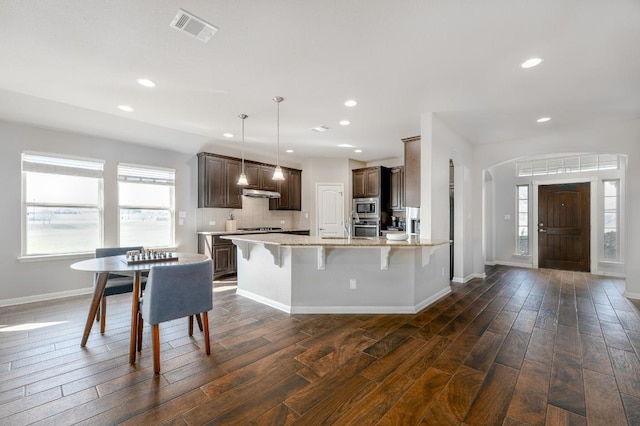 kitchen with dark brown cabinetry, visible vents, dark wood-style floors, a kitchen breakfast bar, and stainless steel appliances