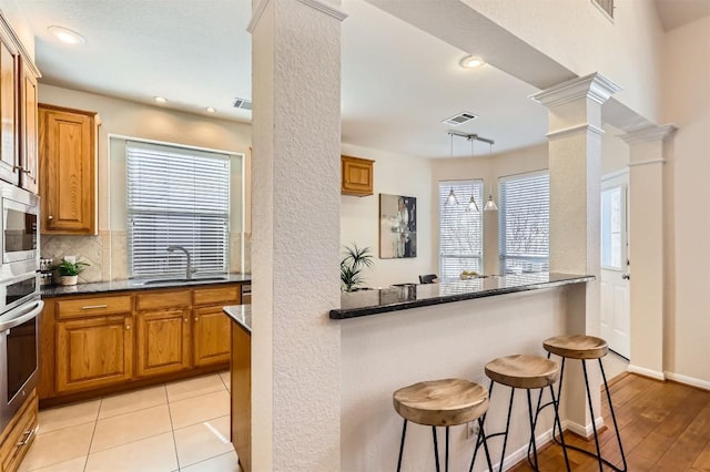 kitchen with decorative columns, stainless steel appliances, visible vents, decorative backsplash, and a sink