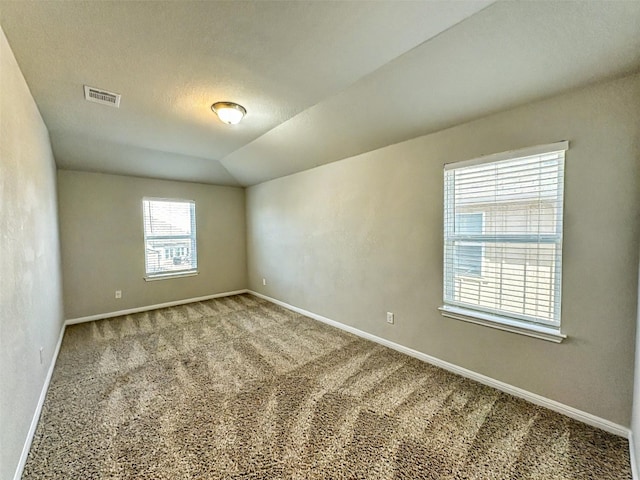 carpeted empty room with visible vents, vaulted ceiling, a textured ceiling, and baseboards