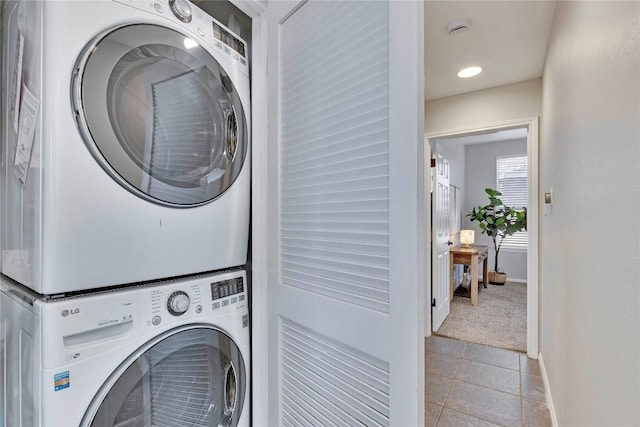 laundry area with light tile patterned floors, stacked washer / dryer, light carpet, laundry area, and baseboards