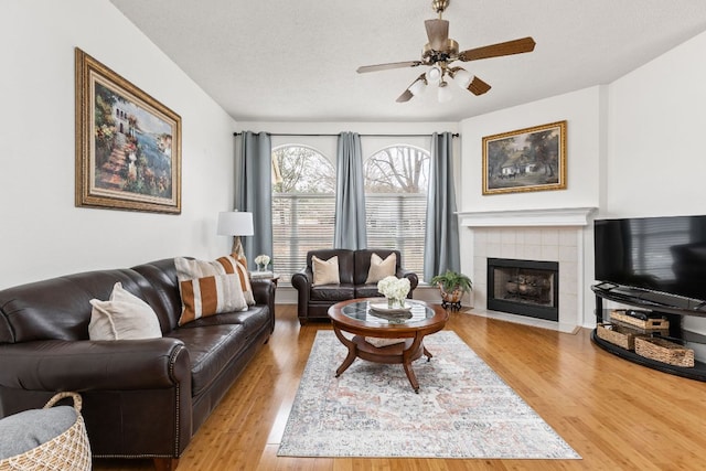 living room with a ceiling fan, a textured ceiling, a tiled fireplace, and wood finished floors