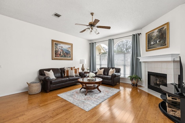 living area with visible vents, a ceiling fan, a textured ceiling, light wood-style floors, and a fireplace