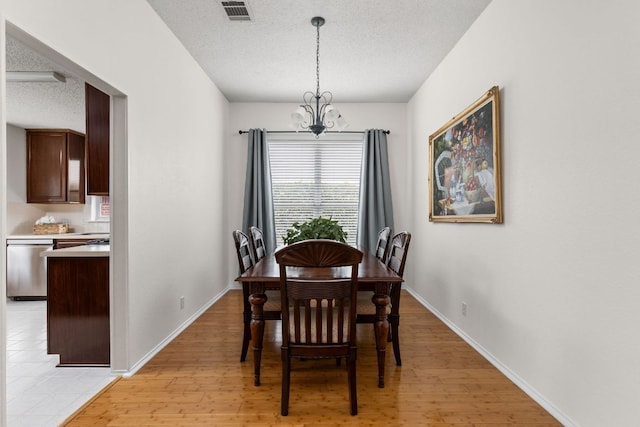 dining room featuring a textured ceiling, baseboards, a chandelier, and light wood-style floors