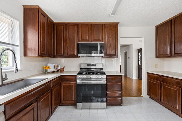 kitchen with light tile patterned floors, a sink, light countertops, appliances with stainless steel finishes, and backsplash