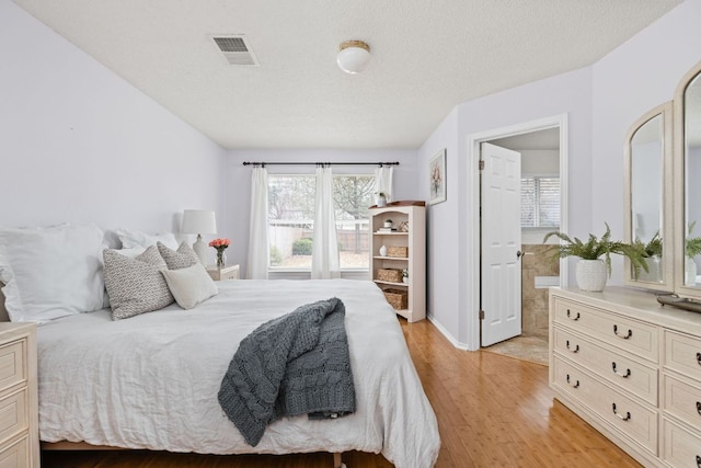 bedroom with a textured ceiling, light wood-style flooring, and visible vents