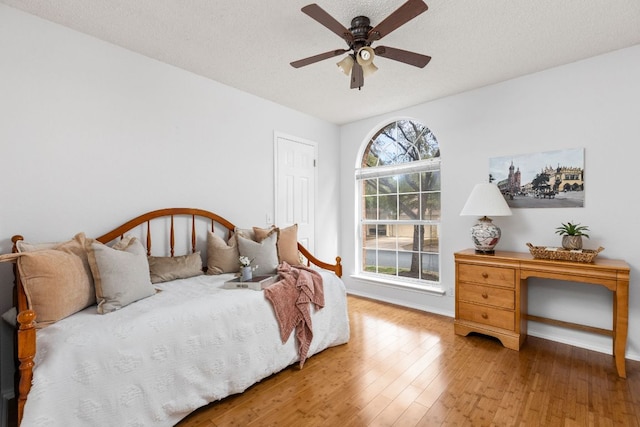 bedroom with ceiling fan, a textured ceiling, baseboards, and wood finished floors