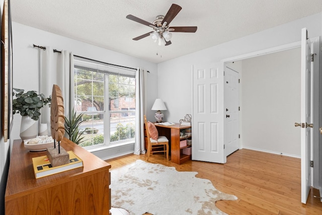 office area with a ceiling fan, light wood-style flooring, baseboards, and a textured ceiling