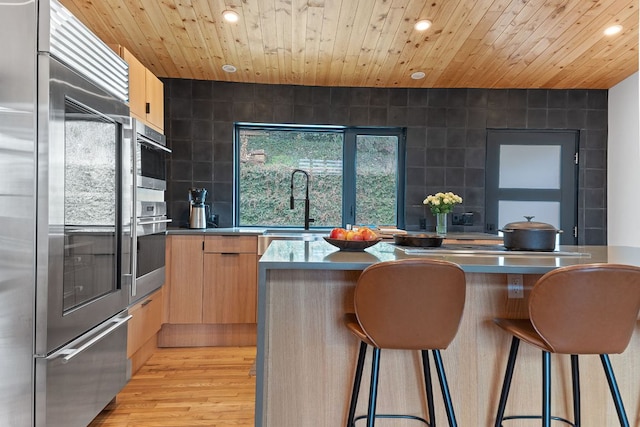 kitchen featuring a breakfast bar, wood ceiling, tile walls, appliances with stainless steel finishes, and modern cabinets