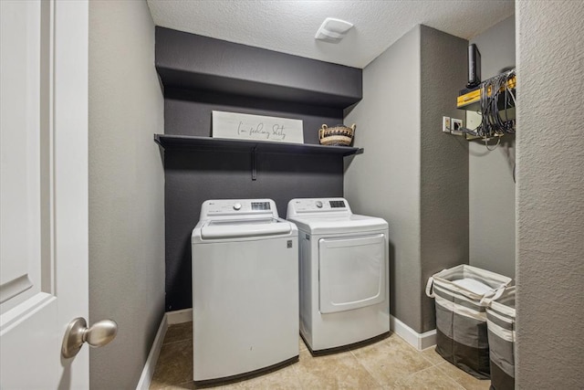 washroom with a textured ceiling, a textured wall, washing machine and dryer, laundry area, and baseboards