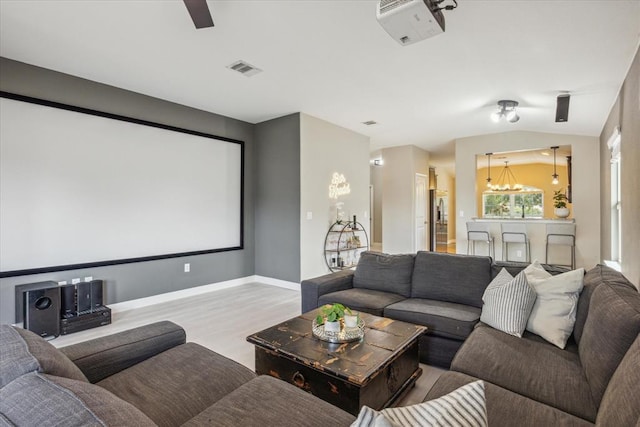 home theater featuring vaulted ceiling, light wood-style flooring, baseboards, a notable chandelier, and visible vents