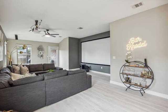 cinema room with light wood-style flooring, visible vents, a ceiling fan, and baseboards