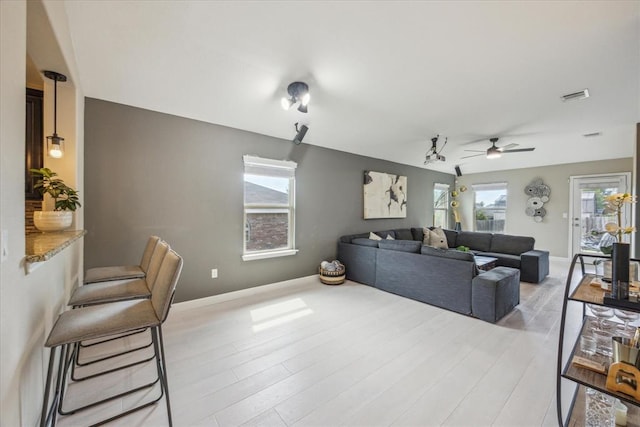 living room with light wood-style floors, visible vents, baseboards, and ceiling fan