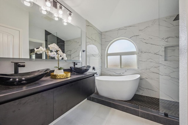 bathroom featuring tile walls, double vanity, lofted ceiling, a sink, and a freestanding tub