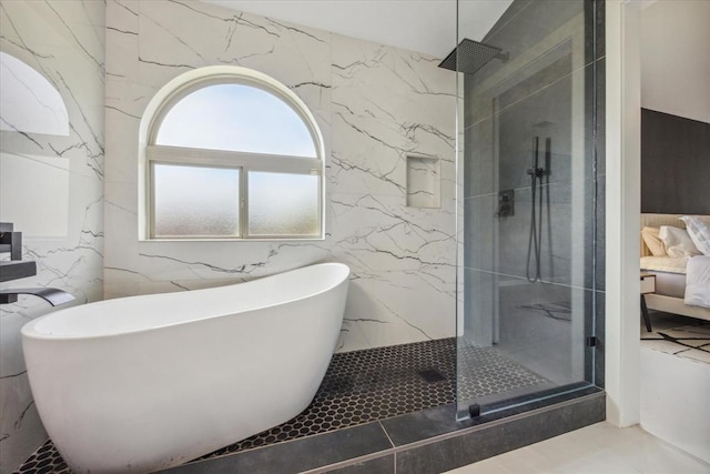 full bathroom with a marble finish shower, a soaking tub, ensuite bath, tile patterned flooring, and stone wall