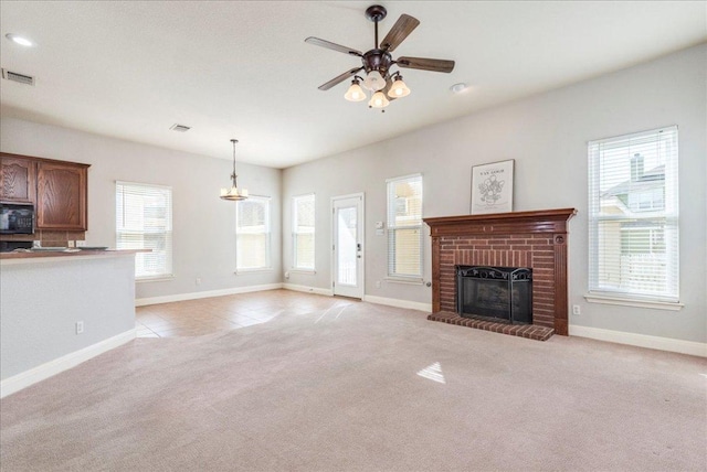 unfurnished living room featuring a ceiling fan, a fireplace, visible vents, and light colored carpet