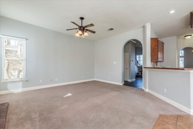 unfurnished living room with carpet floors, plenty of natural light, visible vents, and arched walkways