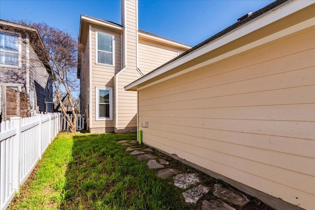 view of home's exterior featuring a yard, a chimney, and fence