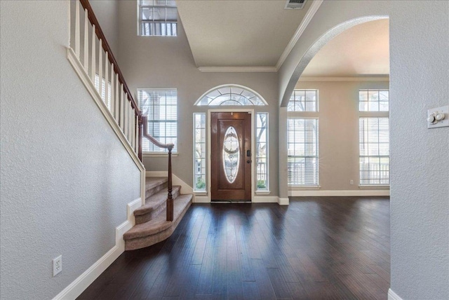 foyer entrance with baseboards, arched walkways, a textured wall, dark wood-style flooring, and crown molding