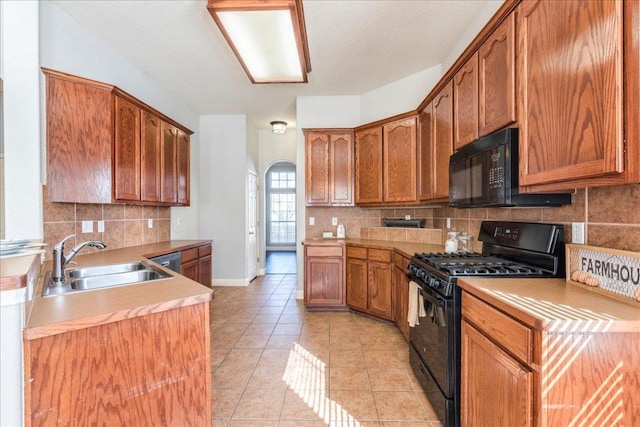 kitchen featuring light tile patterned floors, arched walkways, brown cabinetry, black appliances, and a sink