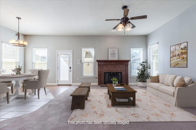 carpeted living area with ceiling fan with notable chandelier, a brick fireplace, baseboards, and tile patterned floors