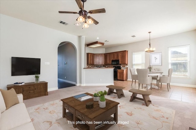 living area with arched walkways, light carpet, a ceiling fan, visible vents, and baseboards