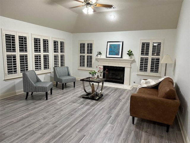 interior space featuring baseboards, a fireplace with raised hearth, a ceiling fan, lofted ceiling, and wood finished floors