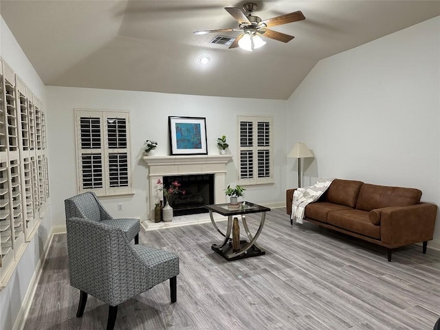 living area with lofted ceiling, visible vents, a fireplace with raised hearth, and wood finished floors