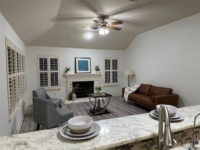 living room with ceiling fan, a fireplace with raised hearth, vaulted ceiling, and wood finished floors