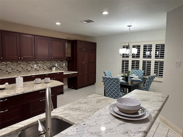 kitchen featuring decorative light fixtures, tasteful backsplash, visible vents, glass insert cabinets, and light tile patterned flooring