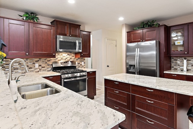 kitchen featuring stainless steel appliances, backsplash, a sink, a kitchen island, and light stone countertops