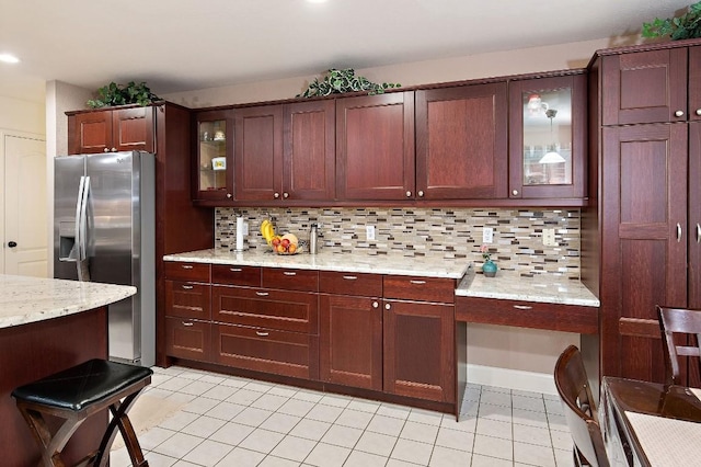 kitchen with light tile patterned floors, backsplash, glass insert cabinets, and stainless steel fridge with ice dispenser