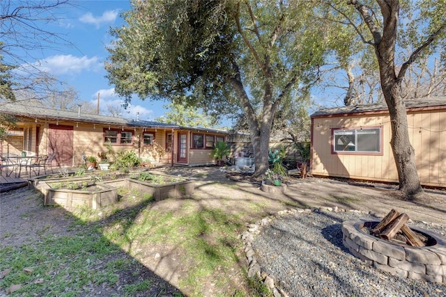 back of house with an outdoor fire pit and a garden